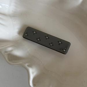 Detail of grey acetate hair clip with floral rhinestone inlay on a white ceramic tray