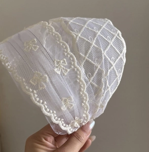 Detailed close-up of beige floral lace headband with pearl accents and intricate mesh embroidery
