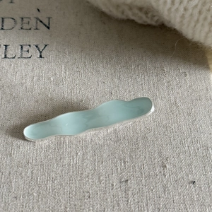 Minimalist mint green wave metal hair clip with gold finish on textured beige linen cloth