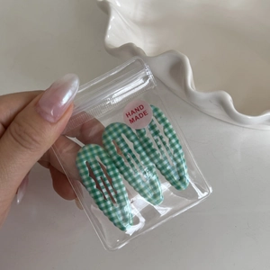 Detailed view of three green plaid wave snap clips in clear hand made packaging
