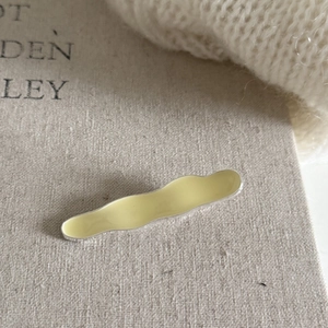 Detail of a wavy cream-colored enamel metal hair clip on a minimalist textured fabric background