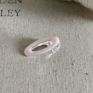 Detailed view of an oval pink enamel hair clip on a natural textured beige fabric