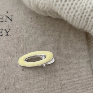 Detailed view of light yellow oval metal hair clip on grey linen background texture
