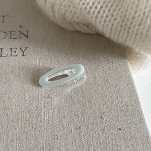 Macro detail of oval mint green enamel hair clip on a textured fabric background