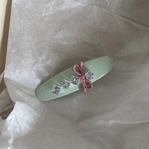 Detailansicht der mintgrünen Haarklammer mit rosa Schleife und Strasssteinen auf Papier