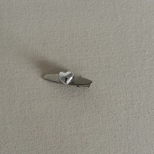 Detailed view of silver heart-shaped hair clip with polished finish on linen fabric