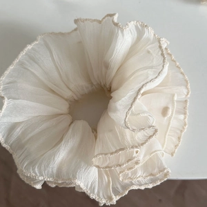 Detail of a creamy white layered tulle scrunchie with delicate wavy lace embroidery edges