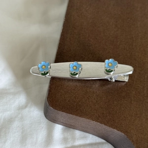Macro detail of a silver hair clip featuring three blue floral accents on a textured surface