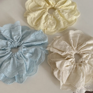 Détail de trois chouchous avec broderie anglaise en bleu clair, jaune doux et crème