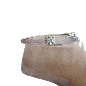 Silver vintage flower hair clip with matte finish and blue crystal center on a stand