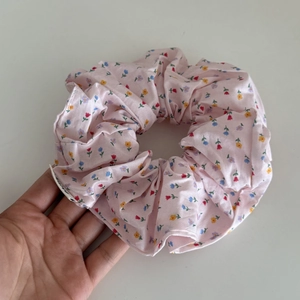 Detailed macro view of a light pink floral scrunchie held by hand for scale reference