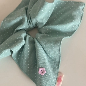 Detailed view of mint green polka dot scrunchie with a floral button and handmade tag