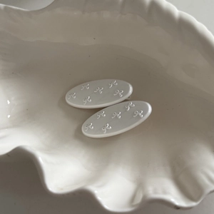 Minimalist white oval hair clips with embossed 3D bow patterns on a ceramic shell tray