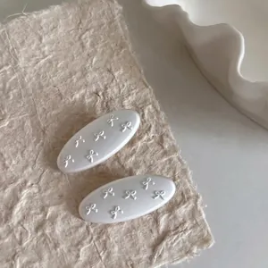 Elegant pair of white oval hair clips with embossed 3D bow design and textured finish