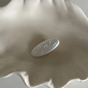 Close-up of minimalist white oval hair clip with embossed bow details on shell dish