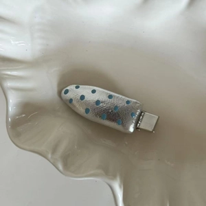 Close-up of silver leather hair clip with blue polka dots on a white ceramic tray