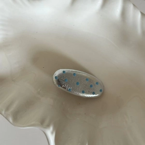 Macro shot of silver metal hair clip with blue enamel dots on a white ceramic tray