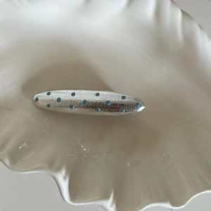 Detail of silver hair clip with blue polka dots on shell-shaped ceramic plate