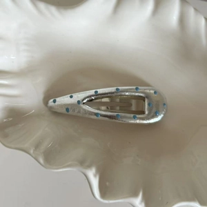 Silver teardrop hair clip with light blue enamel dots in a white shell dish