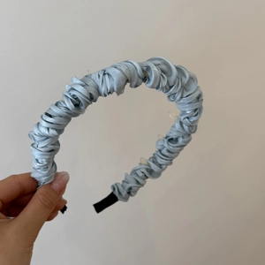 Dettaglio del cerchietto in raso plissettato azzurro con texture morbida e punte antiscivolo