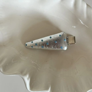 Silver leather hair clip with blue polka dots on a white shell textured tray