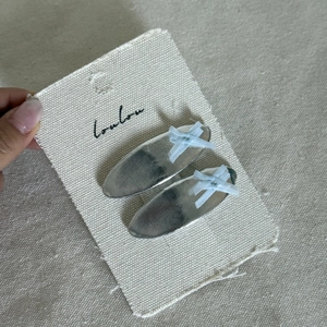 Silver metal oval hair clips set with light blue ribbon bows on cream display card