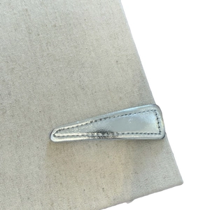 Minimalist silver faux leather triangular hair clip with fine stitching on canvas background