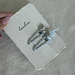 Close-up of silver hair clips with heart charms and blue ribbon on canvas display card