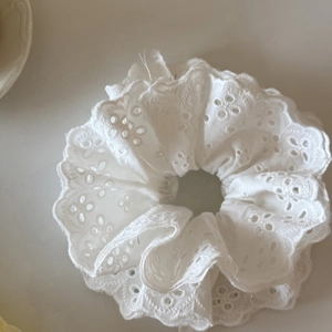 Détail d'un chouchou en dentelle blanche avec broderie florale et bords festonnés