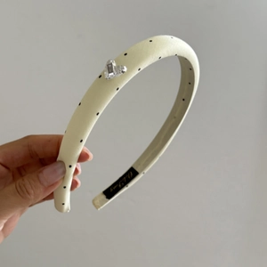 Detail of cream satin polka dot headband featuring a heart crystal and soft fabric texture