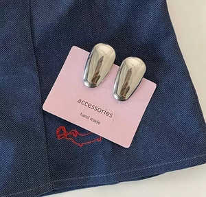 Detailed close-up of glossy silver teardrop earrings on a pink presentation card