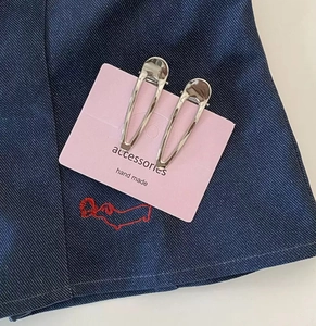 Detail view of two silver metallic teardrop hair clips on pink card packaging
