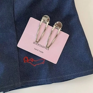 Minimalist silver metal hair clips with polished finish on blue denim background