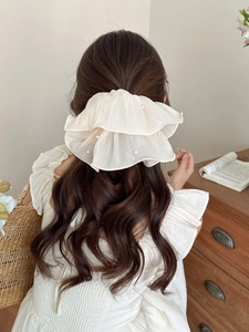 Detailed view of cream ruffled tulle scrunchie with faux pearls on brown wavy hair