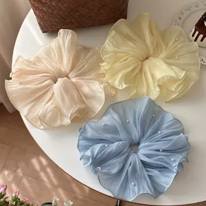 Detail of oversized mesh hair scrunchies with faux pearls in beige, yellow and blue colors