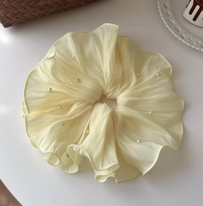 Detail of cream yellow chiffon scrunchie with elegant white pearl beads and ruffled texture