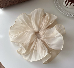 Detail of oversized cream pleated mesh scrunchie with elegant pearls on white background