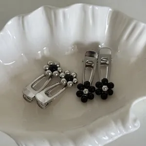 Set of four minimalist silver and black flower hair clips in a white shell-shaped dish