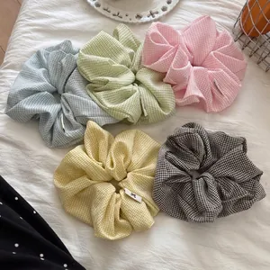 Set of five large gingham check scrunchies in pastel colors on a textured white surface