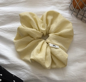 Detail view of yellow gingham scrunchie on white sheet with a black bow tag accent