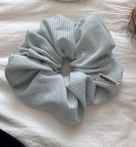 Close-up of light blue gingham scrunchie with soft ruffled fabric and brand woven label