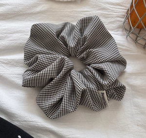 Detail of checkered scrunchie with soft fabric texture and stitched brand label