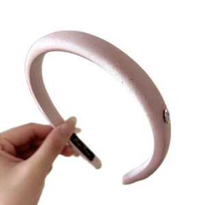 Pink satin padded headband with a silver Love charm shown in a hand-held view