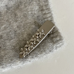 Detail of silver metal hair clip with four flower decorations on gray knit fabric