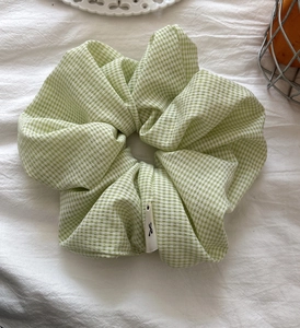 Detail of green and white gingham scrunchie with woven fabric texture and logo label