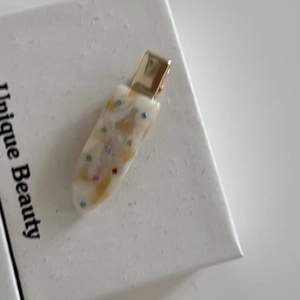 Close-up of cream acetate hair clip with colorful dots and gold duckbill metal base