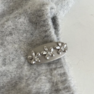 Silver metal floral hair clip on grey plush fabric texture for stylish hair accessory