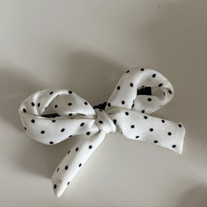 Vue détaillée de dessus d'une barrette noeud en mousseline blanche avec des pois noirs