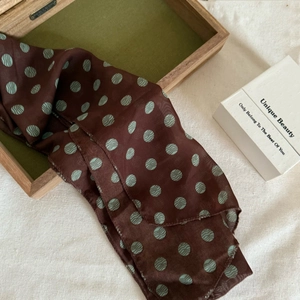 Détail d'un foulard en lin marron à pois vert clair drapé sur une boîte décorative en bois