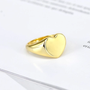 Elegant gold-plated heart signet ring with a polished mirror finish on a minimalist background